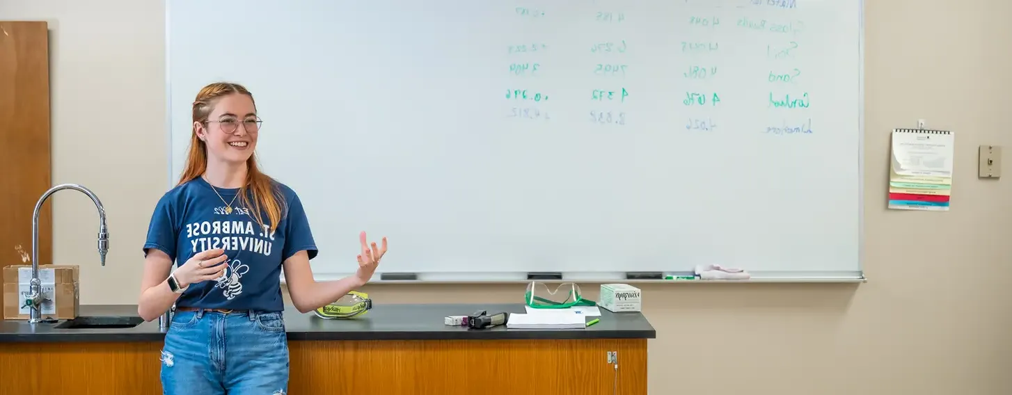 A student standing in front of a whiteboard in a classroom.